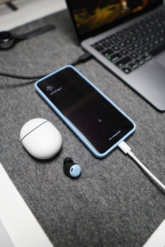 A smartphone charging beside wireless earbuds and a laptop on a tidy desk