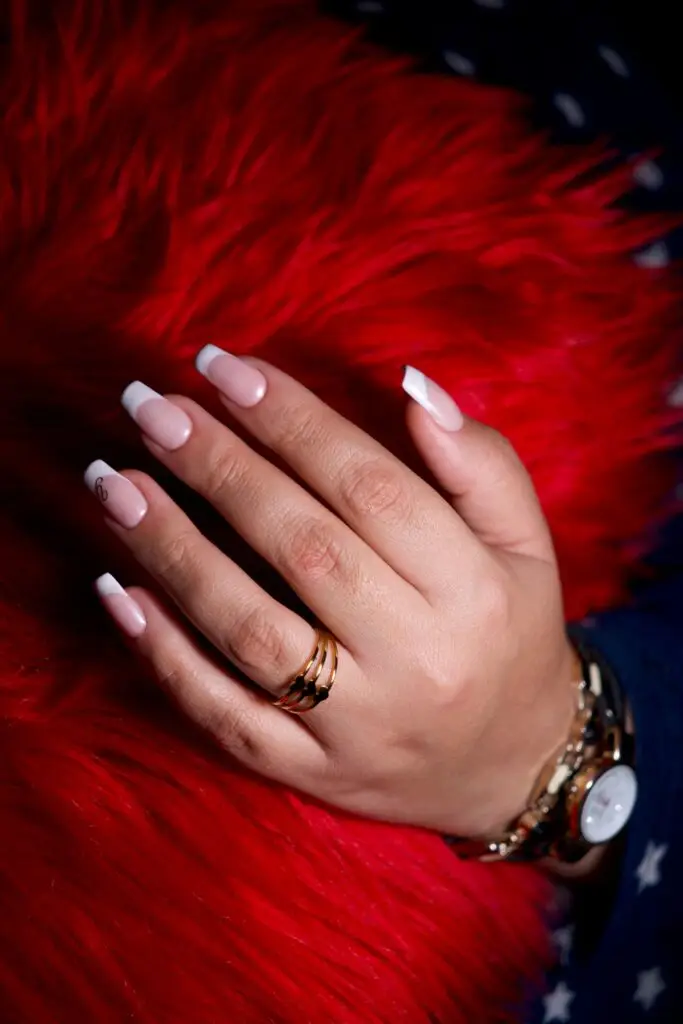 Close-up of a hand with a neat French-style press-on manicure and gold jewelry